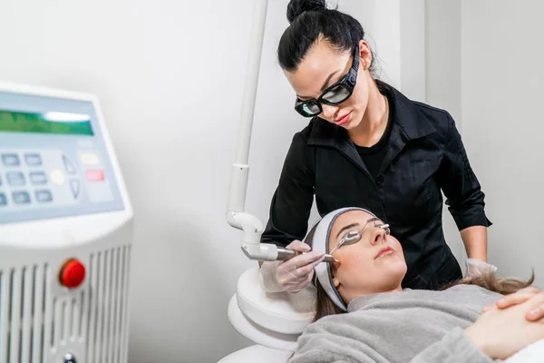 Beauty laser technician performing a cosmetic skin resurfacing session on a female patient, also called a laser peel  or photofacial, with an Er:Yag laser (infrared wavelength). — Stock Photo, Image