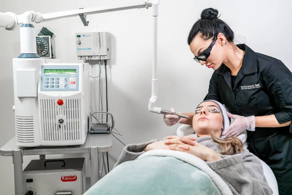 Beauty laser technician performing a cosmetic skin resurfacing session on a female patient, also called a laser peel  or photofacial, with an Er:Yag laser (infrared wavelength).