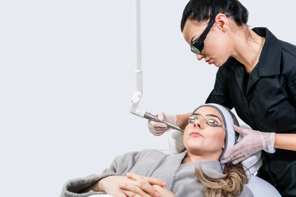 Beauty laser technician performing a cosmetic skin resurfacing session on a female patient, also called a laser peel  or photofacial, with an Er:Yag laser (infrared wavelength). — Stock Photo, Image