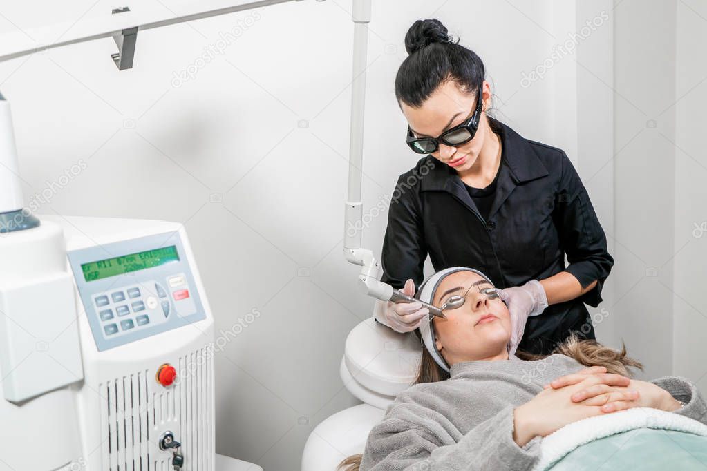 Beauty laser technician performing a cosmetic skin resurfacing session on a female patient, also called a laser peel  or photofacial, with an Er:Yag laser (infrared wavelength).