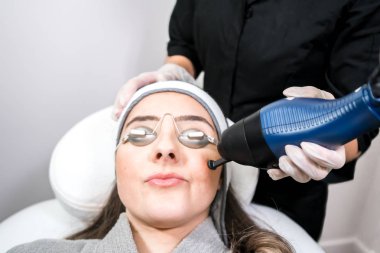 Güzellik lazeri kliniğinde cilt yenilenmesi (cilt yüzeyi) için CO2 fraksiyonel ablatif lazer kullanılır. Güzellik lazeri teknisyeniyle gözlük takan kadın hasta.