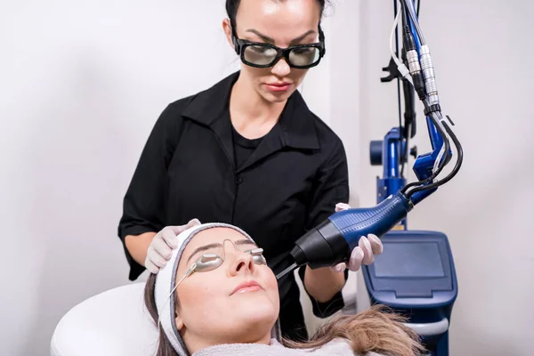 CO2 fractional ablative laser being used for skin rejuvenation (skin resurfacing) as a medical cosmetic procedure in a beauty laser clinic. Female patient wearing goggles, with beauty laser technician — Stock Photo, Image