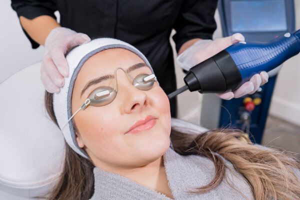 CO2 fractional ablative laser being used for skin rejuvenation (skin resurfacing) as a medical cosmetic procedure in a beauty laser clinic. Female patient wearing goggles, with beauty laser technician