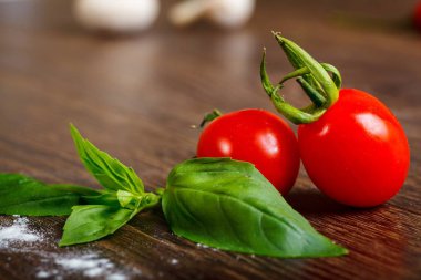 Kahverengi ahşap masada taze kırmızı kiraz domates ve taze yeşil fesleğen yaprakları yakın yukarı