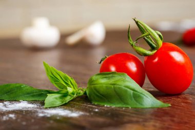 Kahverengi ahşap masada taze kırmızı kiraz domates ve taze yeşil fesleğen yaprakları yakın yukarı
