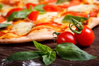 Sıcak kabuk İtalyan Pizza Margherita tarafından dekore kahverengi ahşap masada taze kırmızı kiraz domates ve taze yeşil fesleğen yaprakları yakın yukarı