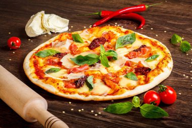 Pizza İtalyan eritilmiş mozzarella peyniri, parmezan peyniri, jambon, erik ve taze yeşil fesleğen yaprakları mozzarella, kırmızı tatlı biber, kiraz domates ve oklava ile dekore kahverengi bir masada