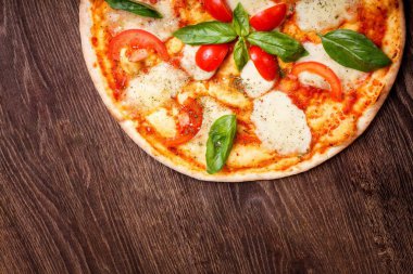 Üst görünüm, erimiş mozzarella peyniri, kırmızı kiraz domates ve taze yeşil fesleğen, mantar, kırmızı tatlı biber ve kiraz ile süslenmiş temiz bir kahverengi masada yaprakları ile Italyan pizza Margherita yakın