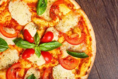 Üst görünüm, erimiş mozzarella peyniri, kırmızı kiraz domates ve taze yeşil fesleğen, mantar, kırmızı tatlı biber ve kiraz ile süslenmiş temiz bir kahverengi masada yaprakları ile Italyan pizza Margherita yakın