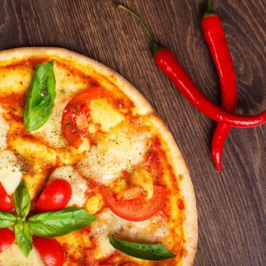 Üst görünüm, erimiş mozzarella peyniri, kırmızı kiraz domates ve taze yeşil fesleğen, mantar, kırmızı tatlı biber ve kiraz ile süslenmiş temiz bir kahverengi masada yaprakları ile Italyan pizza Margherita yakın