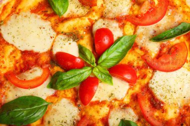 Üst görünüm, erimiş mozzarella peyniri, kırmızı kiraz domates ve taze yeşil fesleğen, mantar, kırmızı tatlı biber ve kiraz ile süslenmiş temiz bir kahverengi masada yaprakları ile Italyan pizza Margherita yakın