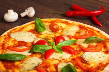Erimiş mozzarella peyniri, kırmızı kiraz domates ve taze yeşil fesleğen, mantar, kırmızı tatlı biber ve kiraz domates ile süslenmiş kahverengi bir masada yaprakları ile Italyan pizza Margherita yakın