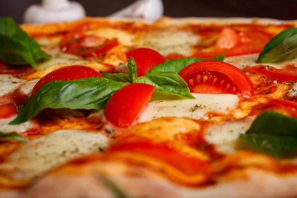 Close up Margherita pizza italiana com queijo mussarela derretido, tomates cereja vermelha e folhas de manjericão verde fresco em uma mesa marrom decorada por cogumelos, pimenta doce vermelha e tomates cereja — Fotografia de Stock