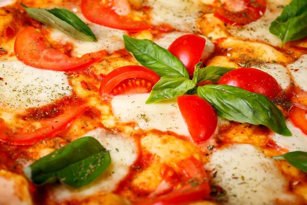Erimiş mozzarella peyniri, kırmızı kiraz domates ve taze yeşil fesleğen, mantar, kırmızı tatlı biber ve kiraz domates ile süslenmiş kahverengi bir masada yaprakları ile Italyan pizza Margherita yakın