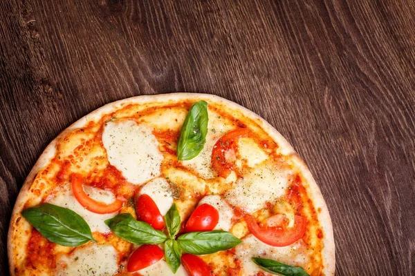 Üst görünüm, erimiş mozzarella peyniri, kırmızı kiraz domates ve taze yeşil fesleğen, mantar, kırmızı tatlı biber ve kiraz ile süslenmiş temiz bir kahverengi masada yaprakları ile Italyan pizza Margherita yakın