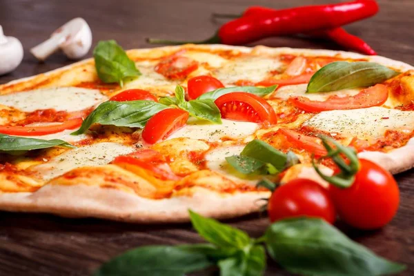 Erimiş mozzarella peyniri, kırmızı kiraz domates ve taze yeşil fesleğen ile pizza Italyan Margherita mantar, kırmızı tatlı biber ve kiraz domates ile süslenmiş kahverengi bir masada yaprakları