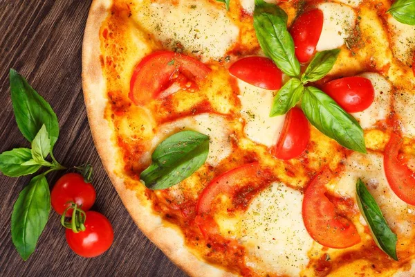 Üst görünüm, erimiş mozzarella peyniri, kırmızı kiraz domates ve taze yeşil fesleğen, mantar, kırmızı tatlı biber ve kiraz ile süslenmiş temiz bir kahverengi masada yaprakları ile Italyan pizza Margherita yakın