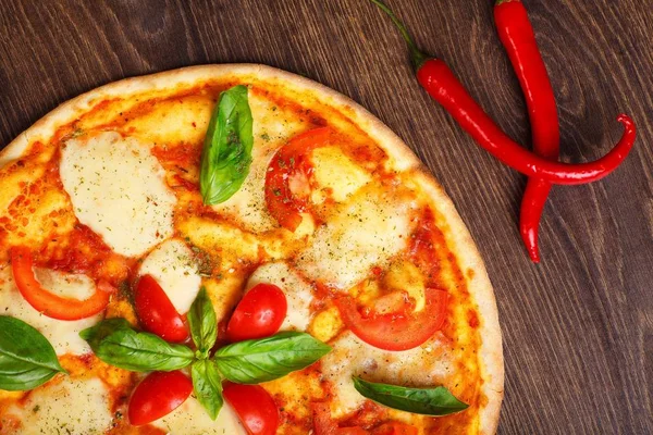 Üst görünüm, erimiş mozzarella peyniri, kırmızı kiraz domates ve taze yeşil fesleğen, mantar, kırmızı tatlı biber ve kiraz ile süslenmiş temiz bir kahverengi masada yaprakları ile Italyan pizza Margherita yakın