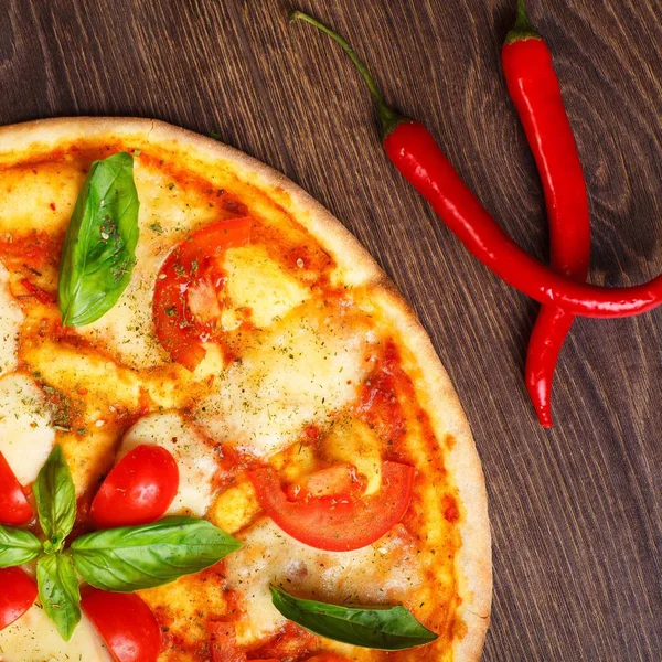 Üst görünüm, erimiş mozzarella peyniri, kırmızı kiraz domates ve taze yeşil fesleğen, mantar, kırmızı tatlı biber ve kiraz ile süslenmiş temiz bir kahverengi masada yaprakları ile Italyan pizza Margherita yakın