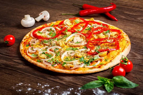 Pizza Italian with melted cheese, red tomatoes, pepper, mushrooms, onion and herbs on a brown table decorated by mushrooms, red sweet pepper and cherry tomatoes — Stock Photo, Image