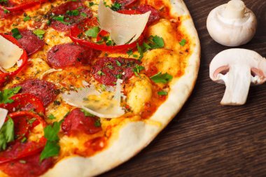 Mantar, kırmızı tatlı biber ve kiraz domates ile süslenmiş kahverengi bir masada parmezan peyniri, domates, salam, pepperoni ve Yeşil fesleğen ile pizza Italyan