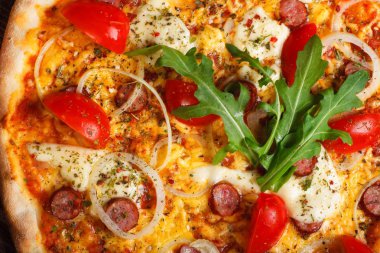 Üst görünüm erimiş mozzarella peyniri ile Italyan pizza yakın, kırmızı kiraz domates, sosis, ve taze yeşil kekik kiraz domates tarafından süslenmiş kahverengi bir masada yaprakları