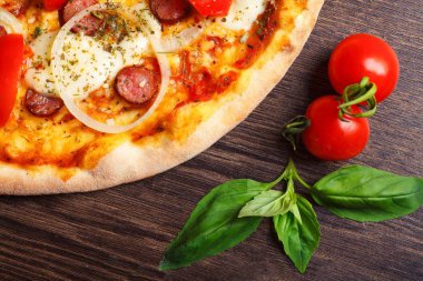 Üst görünüm erimiş mozzarella peyniri ile Italyan pizza yakın, kırmızı kiraz domates, sosis, ve taze yeşil kekik kiraz domates tarafından süslenmiş kahverengi bir masada yaprakları