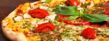 Eritilmiş peynir, kırmızı kiraz domates, tavuk, tavuk ve taze fesleğen yeşil yaprakları ile Italyan pizza yakın mantar, kırmızı tatlı biber ve kiraz domates ile süslenmiş kahverengi bir masada yapraklar