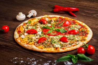 Eritilmiş peynir, kırmızı kiraz domates, tavuk, tavuk ve taze fesleğen yeşil yaprakları ile Italyan pizza yakın mantar, kırmızı tatlı biber ve kiraz domates ile süslenmiş kahverengi bir masada yapraklar