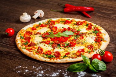 Eritilmiş peynir, sosis, Snack çubukları, biber ve taze yeşil kekik ile Italyan pizza yakın kadar mantar, kırmızı tatlı biber ve kiraz domates ile süslenmiş kahverengi bir masada yaprakları