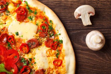 Üst görünüm eritilmiş peynir, sosis, Snack çubukları, biber ve taze yeşil kekik ile Italyan pizza yakın kadar mantar, kırmızı tatlı biber ve kiraz domates ile süslenmiş kahverengi bir masada yaprakları