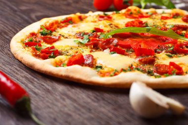 Eritilmiş peynir, sosis, Snack çubukları, biber ve taze yeşil kekik ile Italyan pizza yakın kadar mantar, kırmızı tatlı biber ve kiraz domates ile süslenmiş kahverengi bir masada yaprakları