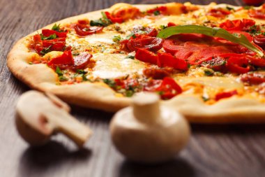 Eritilmiş peynir, sosis, Snack çubukları, biber ve taze yeşil kekik ile Italyan pizza yakın kadar mantar, kırmızı tatlı biber ve kiraz domates ile süslenmiş kahverengi bir masada yaprakları