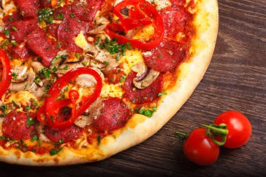 Mantar, kırmızı tatlı biber ve kiraz domates ile süslenmiş kahverengi bir masada eritilmiş peynir, sosis, jambon, salam, mantar, biber ve taze otlar ile üst görünüm Italyan pizza yakın