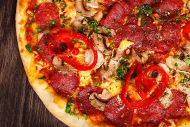 Mantar, kırmızı tatlı biber ve kiraz domates ile süslenmiş kahverengi bir masada eritilmiş peynir, sosis, jambon, salam, mantar, biber ve taze otlar ile üst görünüm Italyan pizza yakın