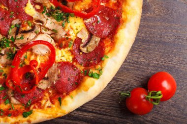 Mantar, kırmızı tatlı biber ve kiraz domates ile süslenmiş kahverengi bir masada eritilmiş peynir, sosis, jambon, salam, mantar, biber ve taze otlar ile üst görünüm Italyan pizza yakın