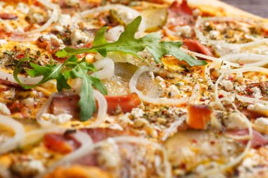 Eritilmiş peynir, mozzarella, jambon, turşu salatalık, soğan ve taze roka yaprakları ile İtalyan pizzası mantar, kırmızı tatlı biber ve kiraz domates ile dekore edilmiş kahverengi bir masaya yakın