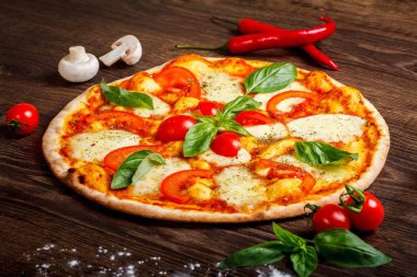 Erimiş mozzarella peyniri, kırmızı kiraz domates ve taze yeşil fesleğen ile pizza Italyan Margherita mantar, kırmızı tatlı biber ve kiraz domates ile süslenmiş kahverengi bir masada yaprakları
