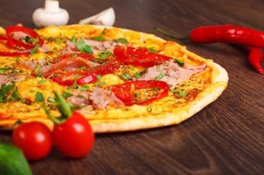 Mantar, kırmızı tatlı biber ve kiraz domates ile süslenmiş kahverengi bir masada jambon, peynir, biber ve otlar ile pizza Italyan