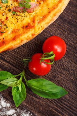 Üst görünüm, taze kırmızı kiraz domates ve taze yeşil fesleğen yaprakları ile süslenmiş kahverengi bir masada jambon, peynir, biber ve otlar ile mantar ve Italyan pizza yakın