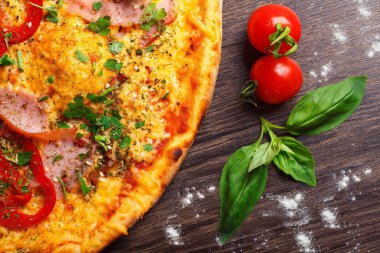 Üst görünüm, taze kırmızı kiraz domates ve taze yeşil fesleğen yaprakları ile süslenmiş kahverengi bir masada jambon, peynir, biber ve otlar ile mantar ve Italyan pizza yakın