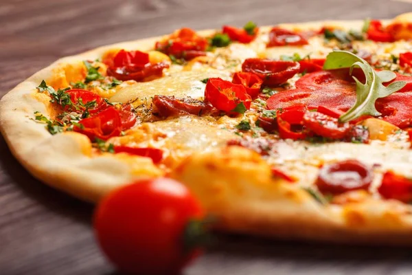 Eritilmiş peynir, sosis, Snack çubukları, biber ve taze yeşil kekik ile Italyan pizza yakın kadar mantar, kırmızı tatlı biber ve kiraz domates ile süslenmiş kahverengi bir masada yaprakları