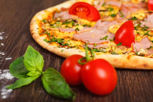Pizza italiana con queso mozzarella derretido, tomates rojos cherry, jamón y hierbas verdes frescas en una mesa marrón decorada con champiñones, pimiento rojo dulce y tomates cherry — Foto de Stock