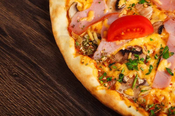 Mantar, kırmızı tatlı biber ve kiraz domates ile süslenmiş kahverengi bir masada erimiş mozzarella peyniri, kırmızı kiraz domates, jambon ve taze yeşil otlar ile üst görünüm Italyan pizza yakın