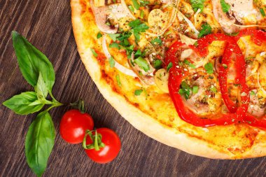 Mantar, kırmızı tatlı biber ve kiraz domates ile süslenmiş kahverengi bir masada eritilmiş peynir, kırmızı domates, biber, mantar, soğan ve otlar ile Italyan pizza yakın