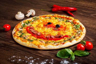 Yakın yukarı görünüm gülümseyen yüz pişmiş peynir ile çocuklar için Italyan pizza, sosis snack çubukları, salam, kırmızı domates ve taze yeşil otlar baharat kahverengi bir tablo mantar ile süslenmiş, kırmızı tatlı