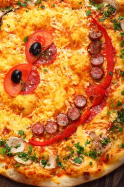 Yakın yukarı görünüm gülümseyen yüz pişmiş peynir ile çocuklar için Italyan pizza, sosis snack çubukları, salam, kırmızı domates ve taze yeşil otlar baharat kahverengi bir tablo mantar ile süslenmiş, kırmızı tatlı