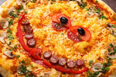 Yakın yukarı görünüm gülümseyen yüz pişmiş peynir ile çocuklar için Italyan pizza, sosis snack çubukları, salam, kırmızı domates ve taze yeşil otlar baharat kahverengi bir tablo mantar ile süslenmiş, kırmızı tatlı