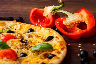 Yakın yukarı vejetaryen ton balığı İtalyan Pizza eritilmiş peynir, siyah zeytin, kırmızı kiraz domates ve taze yeşil fesleğen kahverengi bir masada mantar, siyah zeytin, kırmızı biber ve taze roka ile dekore yaprakları