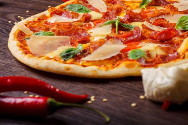 Erimiş mozzarella, parmezan peyniri, salam, kırmızı kiraz domates ve taze yeşil fesleğen ile pizza Italyan mozzarella, kırmızı tatlı biber, kiraz ve haddeleme pin ile dekore kahverengi bir masada yaprakları